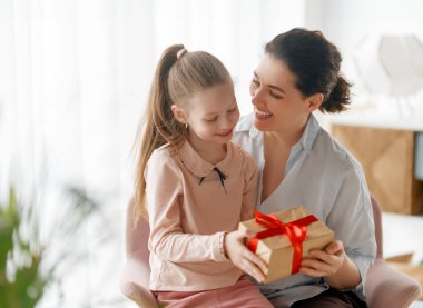 Anneler Günün kutlu olsun. Çocuk kızı annemi tebrik ediyor ve ona hediye paketi veriyor. Anne ve kız gülümsüyor ve sarılıyorlar. Aile tatili ve birliktelik.