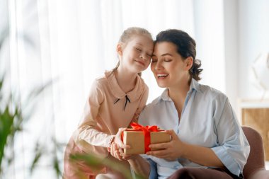 Anneler Günün kutlu olsun. Çocuk kızı annemi tebrik ediyor ve ona hediye paketi veriyor. Anne ve kız gülümsüyor ve sarılıyorlar. Aile tatili ve birliktelik.
