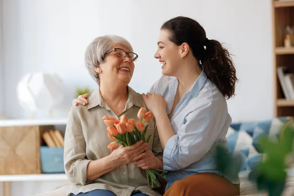 stock image Beautiful young woman and her mother with flowers tulips in hands at home.  