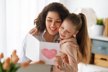Anneler Günün kutlu olsun. Çocuk kızı annemi tebrik ediyor ve ona kartpostal veriyor. Anne ve kız gülümsüyor ve sarılıyorlar. Aile tatili ve birliktelik.