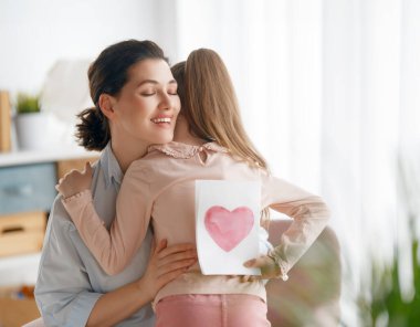 Anneler Günün kutlu olsun. Çocuk kızı annemi tebrik ediyor ve ona kartpostal veriyor. Anne ve kız gülümsüyor ve sarılıyorlar. Aile tatili ve birliktelik.