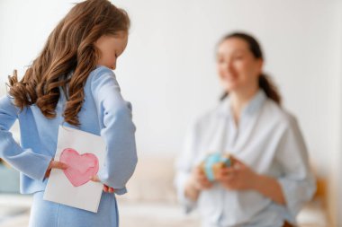 Anneler Günün kutlu olsun. Çocuk kızı annemi tebrik ediyor ve ona kartpostal veriyor. Anne ve kız gülümsüyor. Aile tatili ve birliktelik.