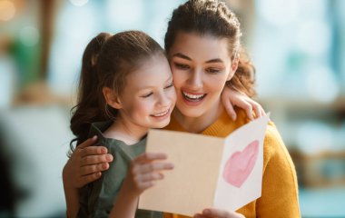 Anneler Günün kutlu olsun. Çocuk kızı annemi tebrik ediyor ve ona kartpostal veriyor. Anne ve kız gülümsüyor ve sarılıyorlar. Aile tatili ve birliktelik.