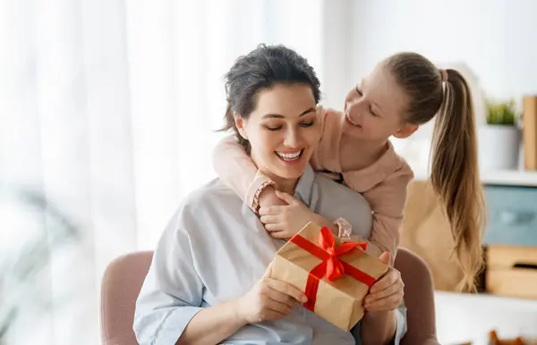 Stock image Happy mother's day. Child daughter is congratulating mom and giving her gift box. Mum and girl smiling and hugging. Family holiday and togetherness.