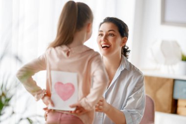 Anneler Günün kutlu olsun. Çocuk kızı annemi tebrik ediyor ve ona kartpostal veriyor. Anne ve kız gülümsüyor ve sarılıyorlar. Aile tatili ve birliktelik.