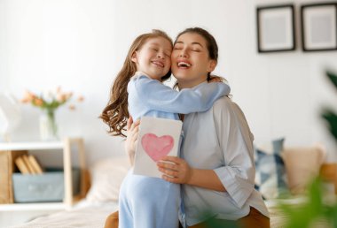Anneler Günün kutlu olsun. Çocuk kızı annemi tebrik ediyor ve ona kartpostal veriyor. Anne ve kız gülümsüyor ve sarılıyorlar. Aile tatili ve birliktelik.