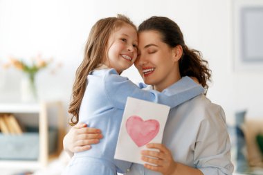Anneler Günün kutlu olsun. Çocuk kızı annemi tebrik ediyor ve ona kartpostal veriyor. Anne ve kız gülümsüyor ve sarılıyorlar. Aile tatili ve birliktelik.