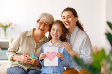 Anneler Günün kutlu olsun. Çocuk, anne ve babaanne. Posta kutusu ve kartpostalları var. Büyükanne, anne ve kız gülümsüyor. Aile tatili ve birliktelik.