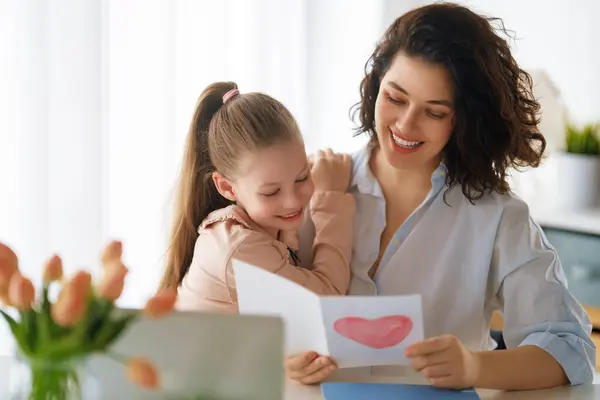 母亲节快乐 孩子的女儿正在向妈妈道贺 并给她寄明信片 妈妈和女孩笑着和拥抱 家庭假日和团聚 免版税图库照片