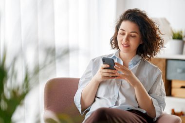 Mutlu, sıradan, güzel bir kadın telefonuyla evdeki koltukta oturuyor..