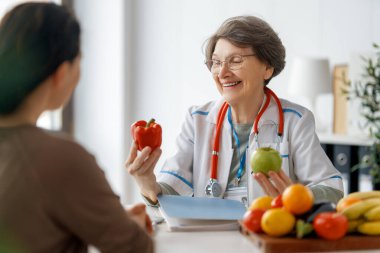 Mutlu doktor ilaç ofisinde çalışıyor. Bir kadın, bir hastayla meyve ve sebze yemenin önemi hakkında konuşuyor..