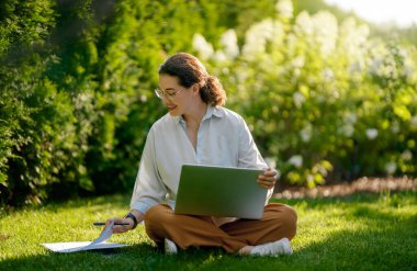 Mutlu kadın yaz sabahı dizüstü bilgisayarda çalışıyor bahçede oturuyor..