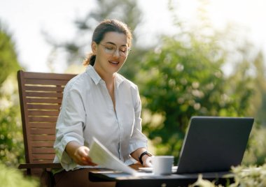 Mutlu kadın yaz sabahı dizüstü bilgisayarda çalışıyor bahçede oturuyor..