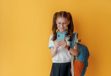 Parlak sarı arka planda duran sevimli mutlu ergen. Sırt çantalı çocuk, kız okula dönmeye hazır..