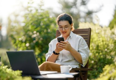 Mutlu kadın yaz sabahı dizüstü bilgisayarda çalışıyor bahçede oturuyor..