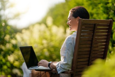 Mutlu kadın yaz sabahı dizüstü bilgisayarda çalışıyor bahçede oturuyor..