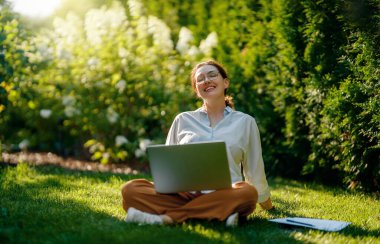 Mutlu kadın yaz sabahı dizüstü bilgisayarda çalışıyor bahçede oturuyor..