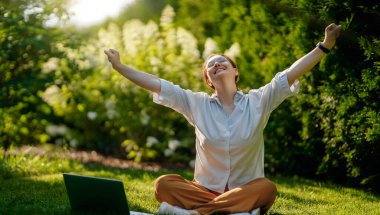 Mutlu kadın yaz sabahı dizüstü bilgisayarda çalışıyor bahçede oturuyor..