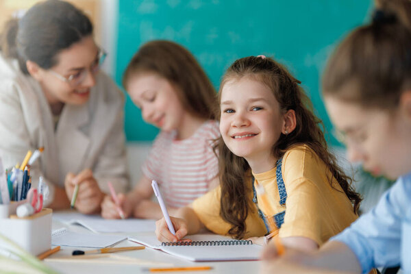 Happy kids and teacher at school. Woman and children are working in the class.