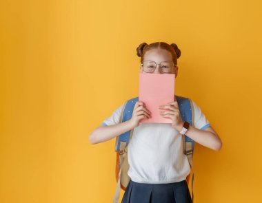 Parlak sarı arka planda duran sevimli mutlu ergen. Sırt çantalı çocuk, kız okula dönmeye hazır.. 