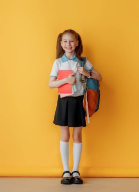 Parlak sarı arka planda duran sevimli mutlu ergen. Sırt çantalı çocuk, kız okula dönmeye hazır.. 