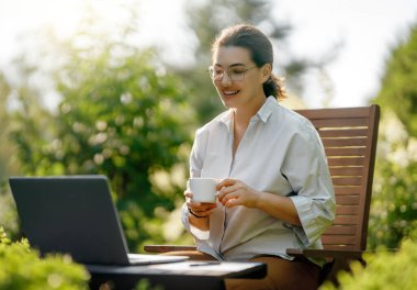 Mutlu kadın yaz sabahı dizüstü bilgisayarda çalışıyor bahçede oturuyor..