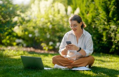Mutlu kadın yaz sabahı dizüstü bilgisayarda çalışıyor bahçede oturuyor..