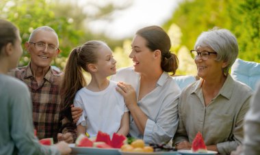 Mutlu aile yaz sabahları birlikte vakit geçirir. Aile bahçede oturuyor ve sohbetin tadını çıkarıyor..