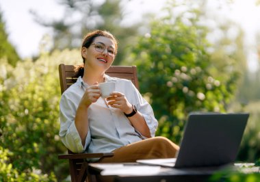 Mutlu kadın yaz sabahı dizüstü bilgisayarda çalışıyor bahçede oturuyor..