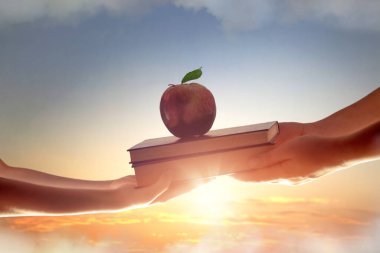 Back to school. Hand of adult giving a book to a child on background of sunset sky. Concept of education and reading. clipart