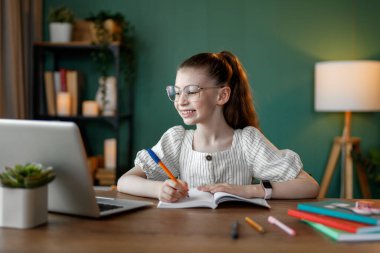 Mutlu çocuk masada oturuyor. Ödev yapan ya da online eğitim alan kız.