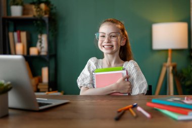 Mutlu çocuk masada oturuyor. Ödev yapan ya da online eğitim alan kız.