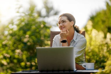 Mutlu kadın yaz sabahı dizüstü bilgisayarda çalışıyor bahçede oturuyor..