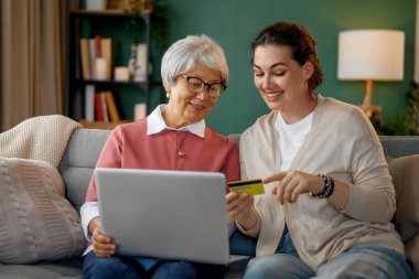 Genç ve yaşlı kadınlar online alışveriş için dizüstü bilgisayar kullanıyorlar. Kızı evde annesine yardım ediyor..