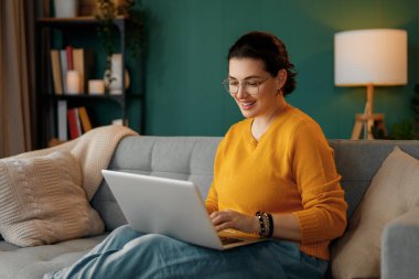 Evde dizüstü bilgisayar kullanan mutlu ve güzel bir kadın..