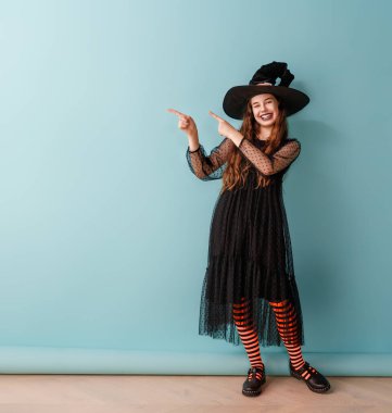 Cadılar Bayramı cadı kostümlü güzel bir kız mavi duvar arkasında.