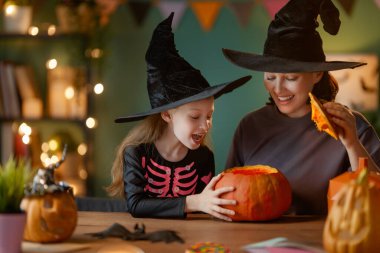 Mutlu aile Cadılar Bayramı için hazırlanıyor. Anne ve çocuk evde balkabağı oyuyor..