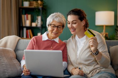 Genç ve yaşlı kadınlar online alışveriş için dizüstü bilgisayar kullanıyorlar. Kızı evde annesine yardım ediyor..