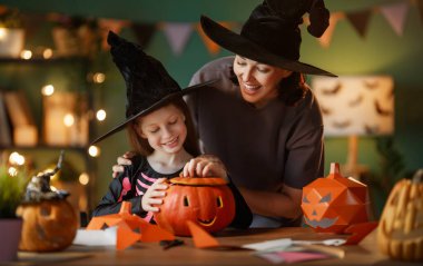 Mutlu aile Cadılar Bayramı için hazırlanıyor. Anne ve çocuk evde balkabağı kesiyor..