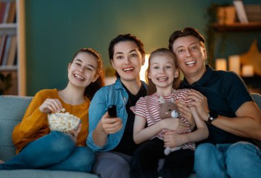 Mutlu aile projektörü, TV, akşam evde patlamış mısırlı filmler. Anne, baba ve kızları birlikte vakit geçiriyorlar..