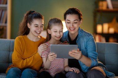 Tablet bilgisayar kullanarak gülümseyen aile evdeki kanepede oturuyor..