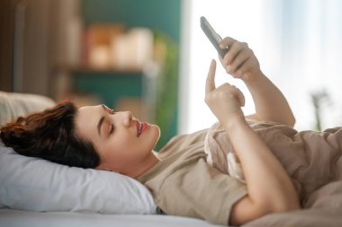 Mutlu, sıradan, güzel bir kadın evdeki yatakta telefon kullanıyor..