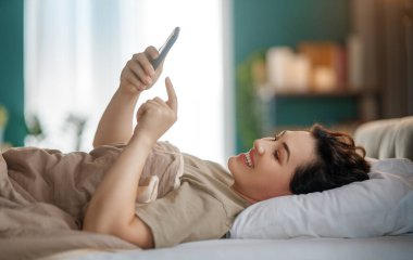 Mutlu, sıradan, güzel bir kadın evdeki yatakta telefon kullanıyor..