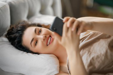 Mutlu, sıradan, güzel bir kadın evdeki yatakta telefon kullanıyor..