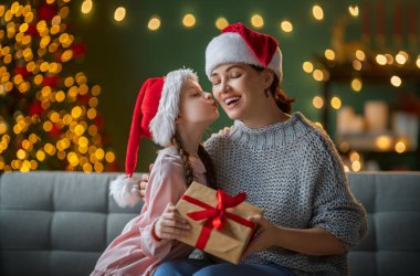 Mutlu Noeller ve mutlu tatiller. Anne ve çocuk hediye değiş tokuşu. Ebeveyn ve kızı içeride ağaç kenarında eğleniyorlar. Odasında hediyeler olan sevgi dolu bir aile.