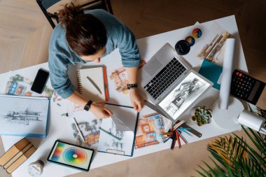 Stüdyoda çalışan dizüstü bilgisayar ve çizimler kullanan tasarımcı.