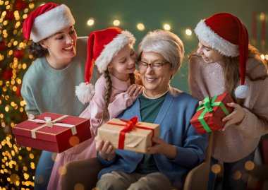Mutlu Noeller ve mutlu tatiller. Büyükanne, anne ve çocuklar hediye değiş tokuşu yapıyor. Ebeveynler ve kızlar kapalı alanda eğleniyorlar. Odasında hediyeler olan sevgi dolu bir aile.