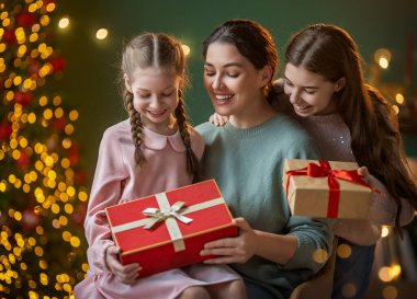Mutlu Noeller ve mutlu tatiller. Anne ve çocuklar hediye değiş tokuşu yapıyor. Ebeveynler ve kızlar içeride ağaçların yanında eğleniyorlar. Odasında hediyeler olan sevgi dolu bir aile.