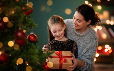 Mutlu Noeller, mutlu tatiller. Anne ve kızı ağacın yanında hediyelerle..