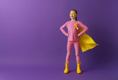 Dünya Çocuk Kanser Günü. Altın kurdeleli süper kahraman kostümlü kız.. 